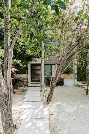 A pathway leading to a modern house with a garage door, surrounded by trees and plants. - 3-bedroom townhome in lovely Tulum with AC and charm (Tulum)