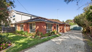 A residential property with a brick exterior, a front yard with a gravel driveway, and a green fence. - Acacia - Point Lonsdale (POINT LONSDALE)