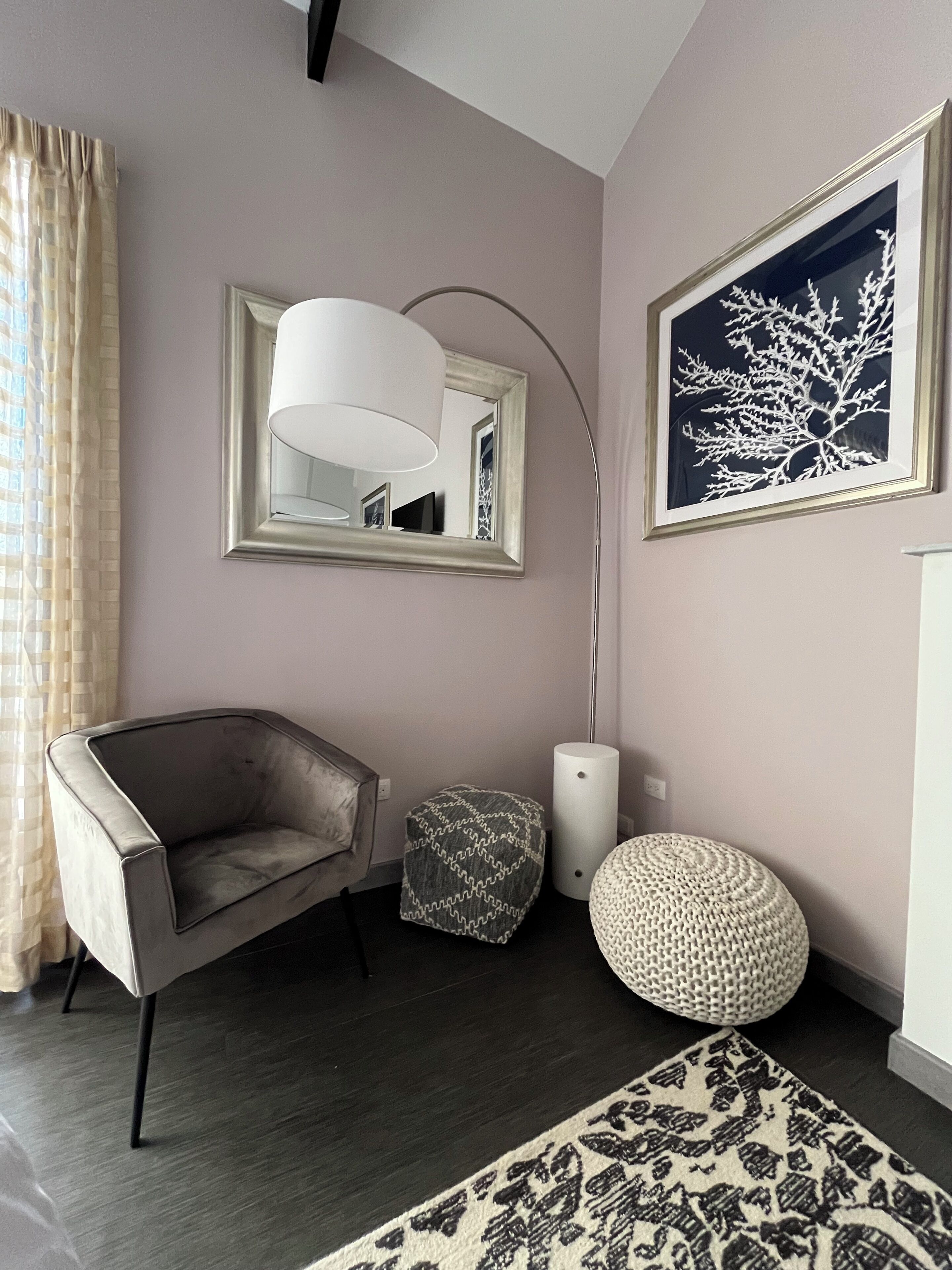 A modern living room with a grey armchair, a small ottoman, a floor lamp, and a framed artwork on the wall.