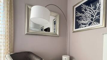 A modern living room with a grey armchair, a small ottoman, a floor lamp, and a framed artwork on the wall.