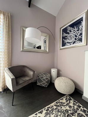 A modern living room with a grey armchair, a small ottoman, a floor lamp, and a framed artwork on the wall.