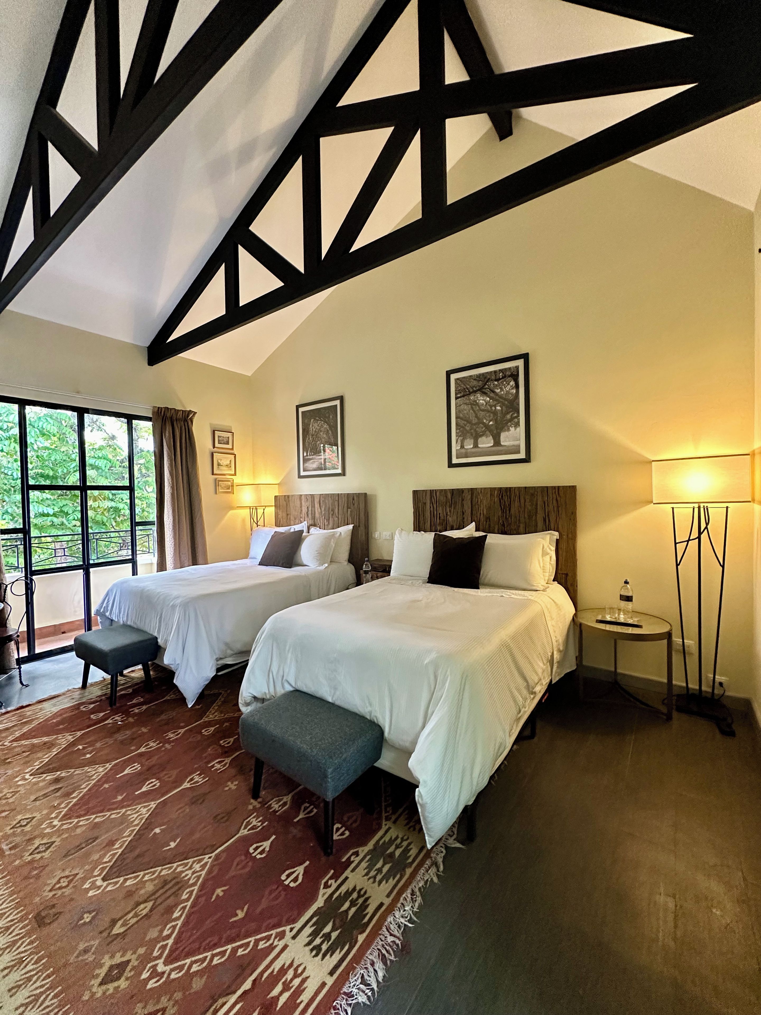 Habitación de hotel con dos camas, un ventanal grande y vistas a zonas verdes.