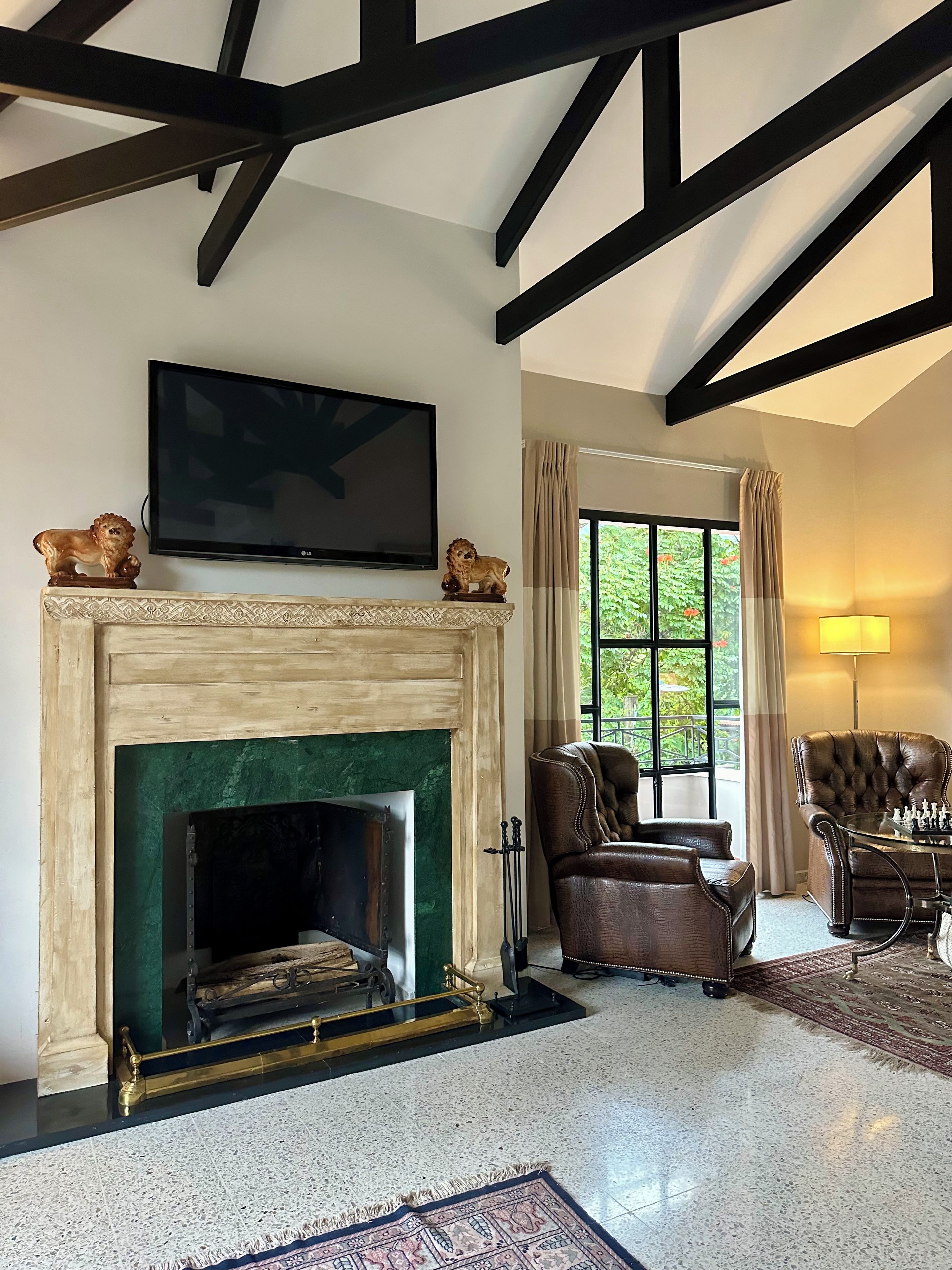 A living room with a fireplace, a television mounted on the wall, leather armchairs, and a chessboard.
