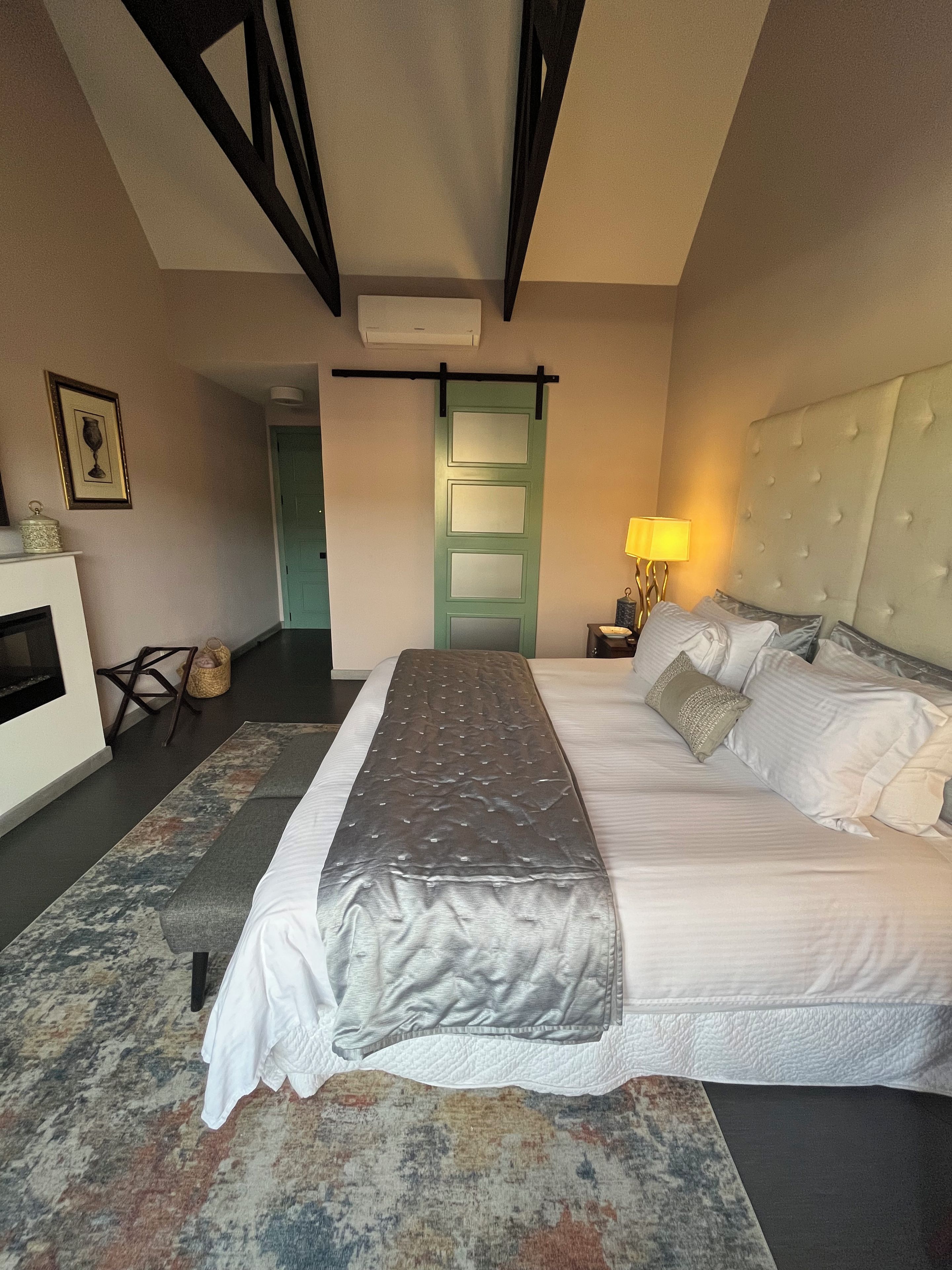 Une chambre à coucher comprenant un lit, une lampe de chevet, un climatiseur fixé au mur, un tableau encadré et une porte.
