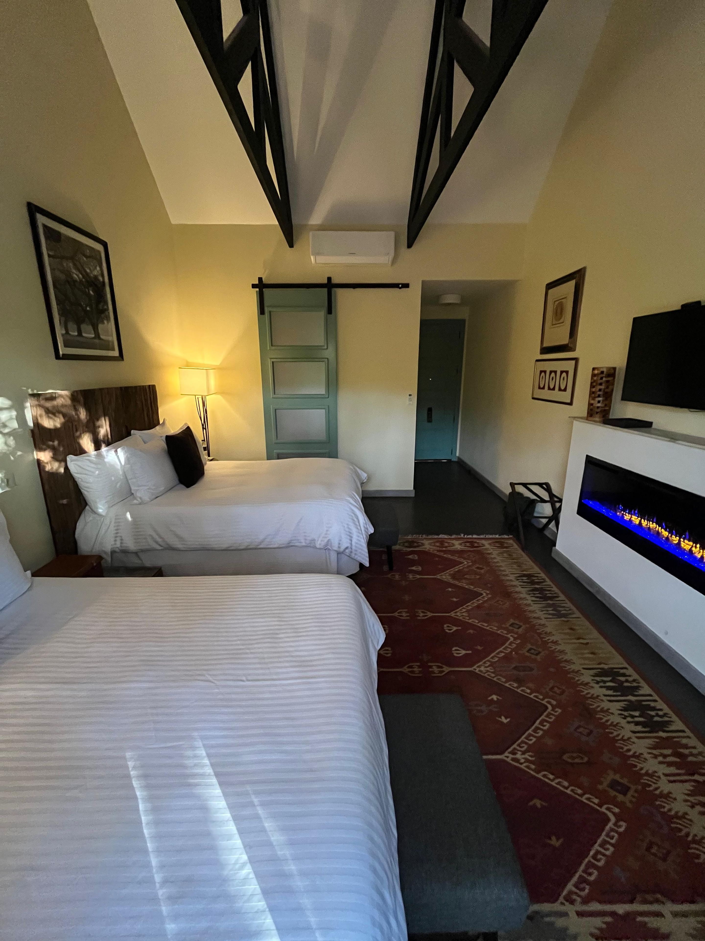 Quarto de hotel com duas camas, televisão, lareira e porta que dá para outro cômodo.