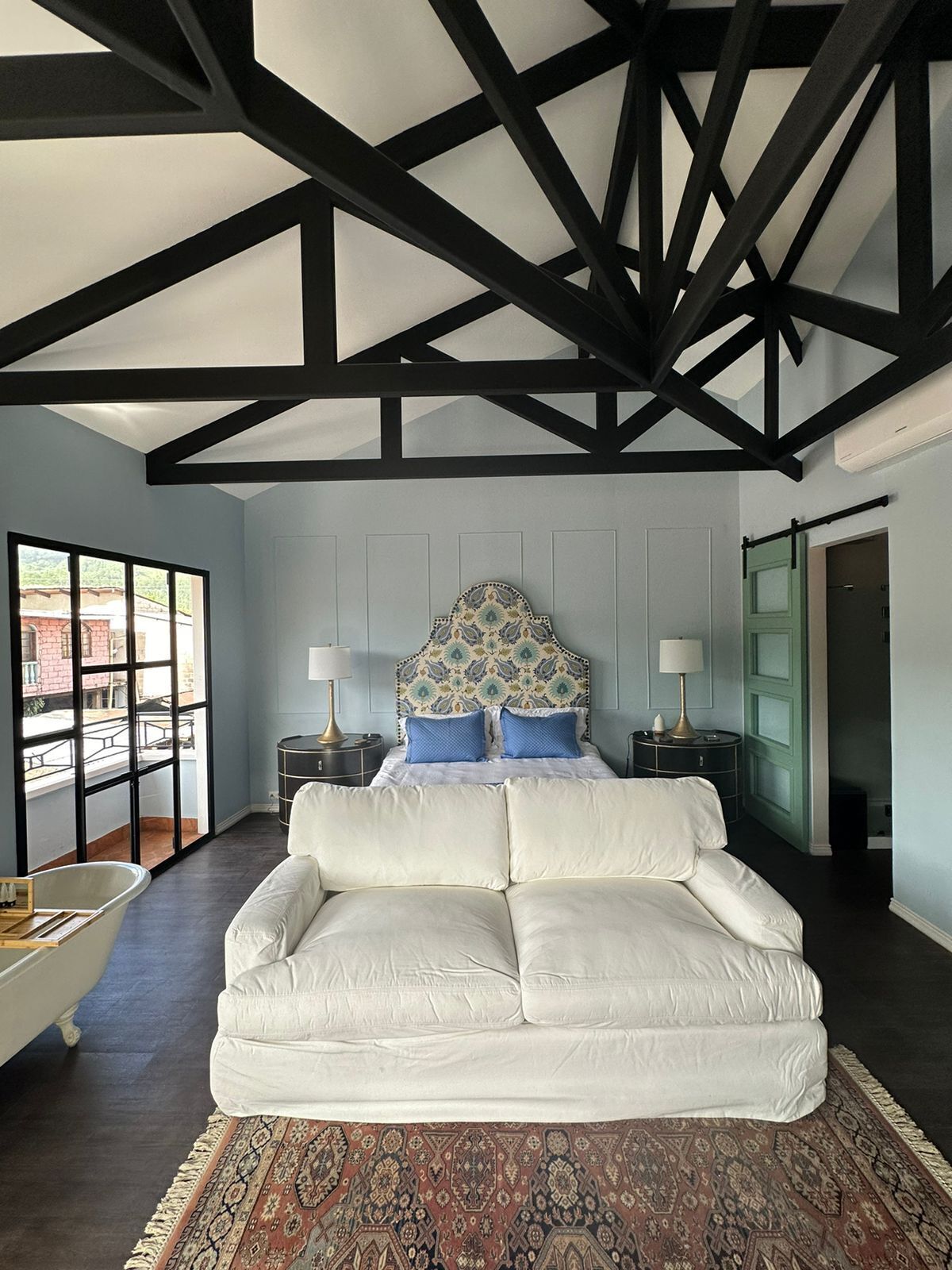 Um quarto moderno com um sofá branco, uma cabeceira estampada e uma janela grande.