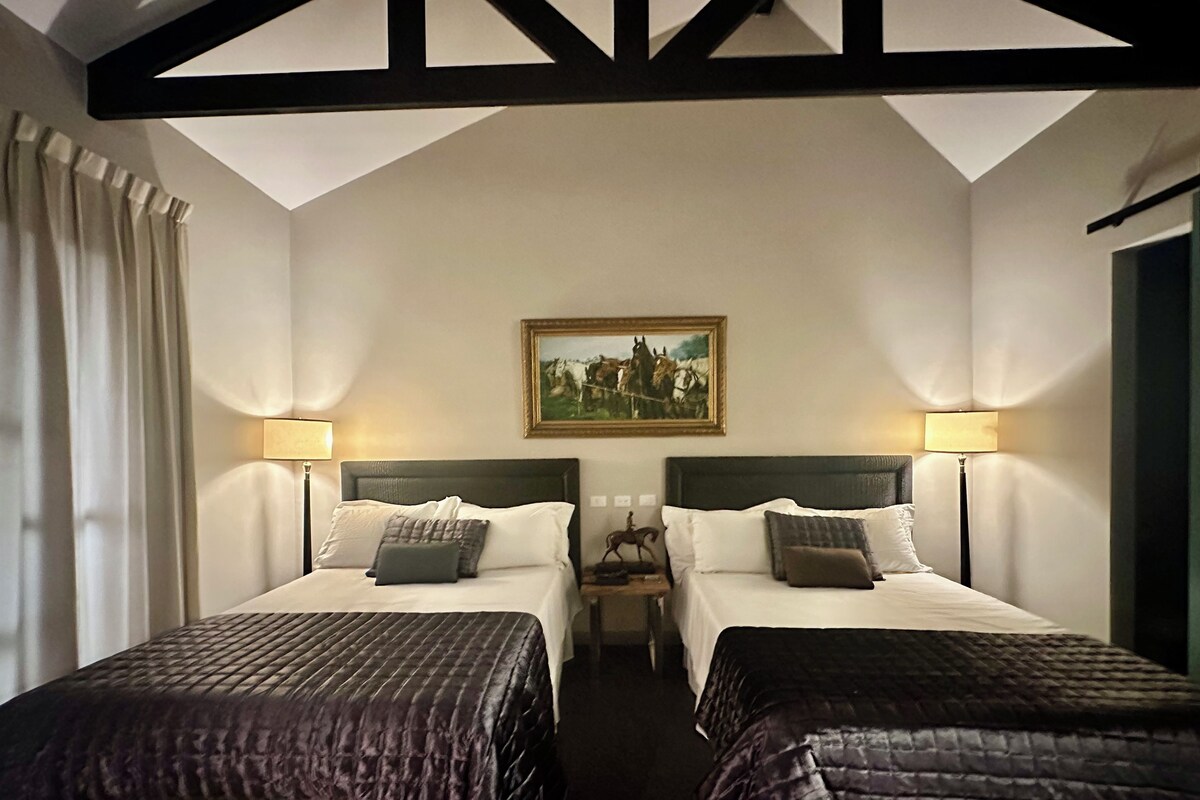 A hotel room with two beds, a painting on the wall, and a ceiling with exposed beams.
