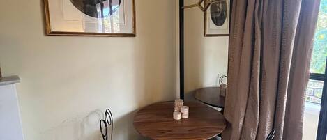 Een kamer met een ronde houten tafel, twee stoelen, een lijst met foto, een spiegel en een raam met gordijnen.