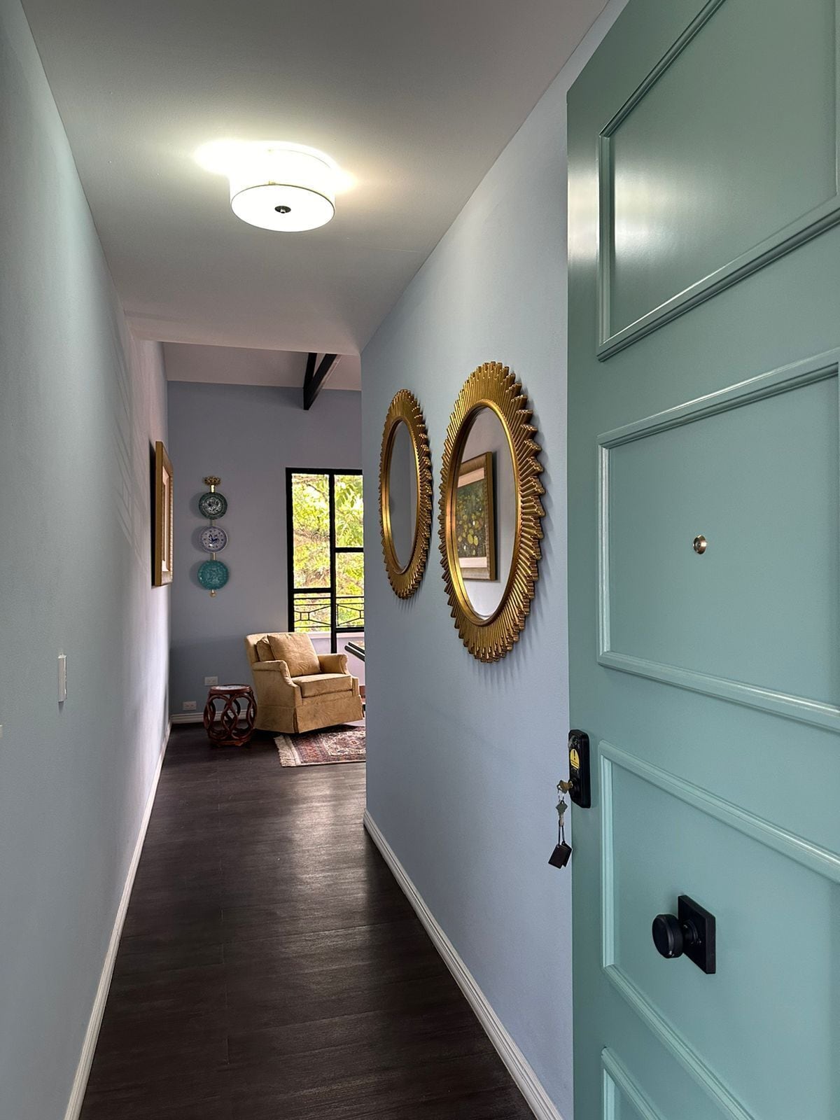 Un pasillo con una puerta azul claro, suelo de madera oscura y dos espejos fijados a la pared.