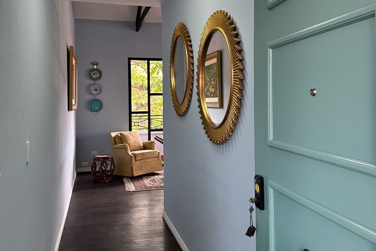 A hallway with a light blue door, dark wooden flooring, and two wall-mounted mirrors.