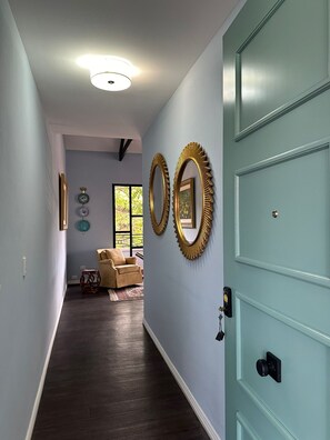 Un pasillo con una puerta azul claro, suelo de madera oscura y dos espejos fijados a la pared.