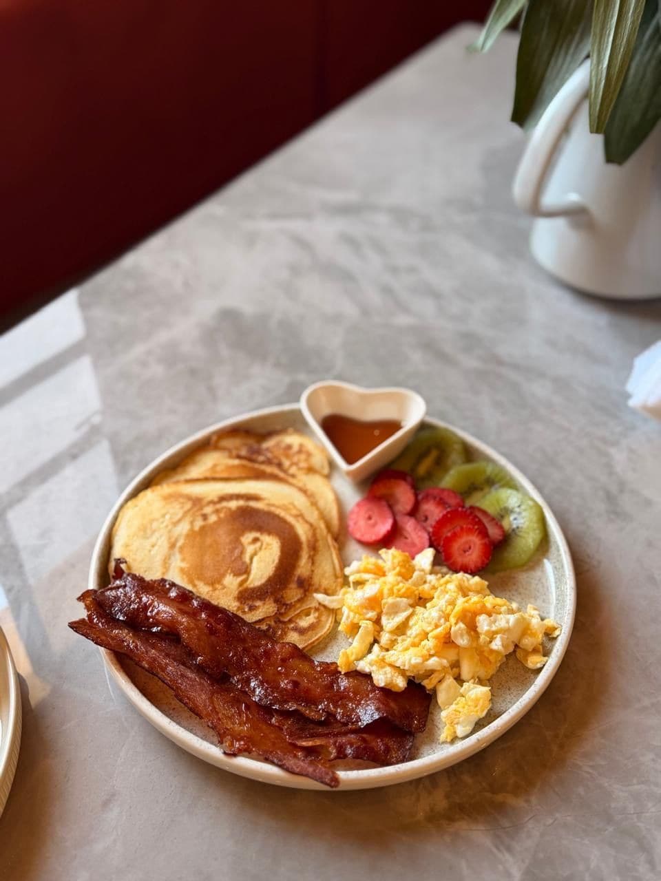 A breakfast plate with pancakes, bacon, scrambled eggs, and fruit.