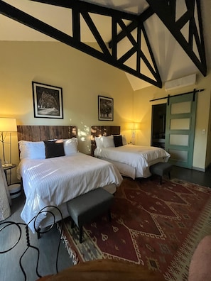 A hotel room with two beds, a bench, a patterned rug, and a wooden ceiling structure.