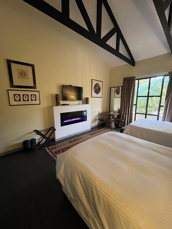 A hotel room with a bed, a flat-screen TV, a fireplace, a dining table, and a window with curtains.