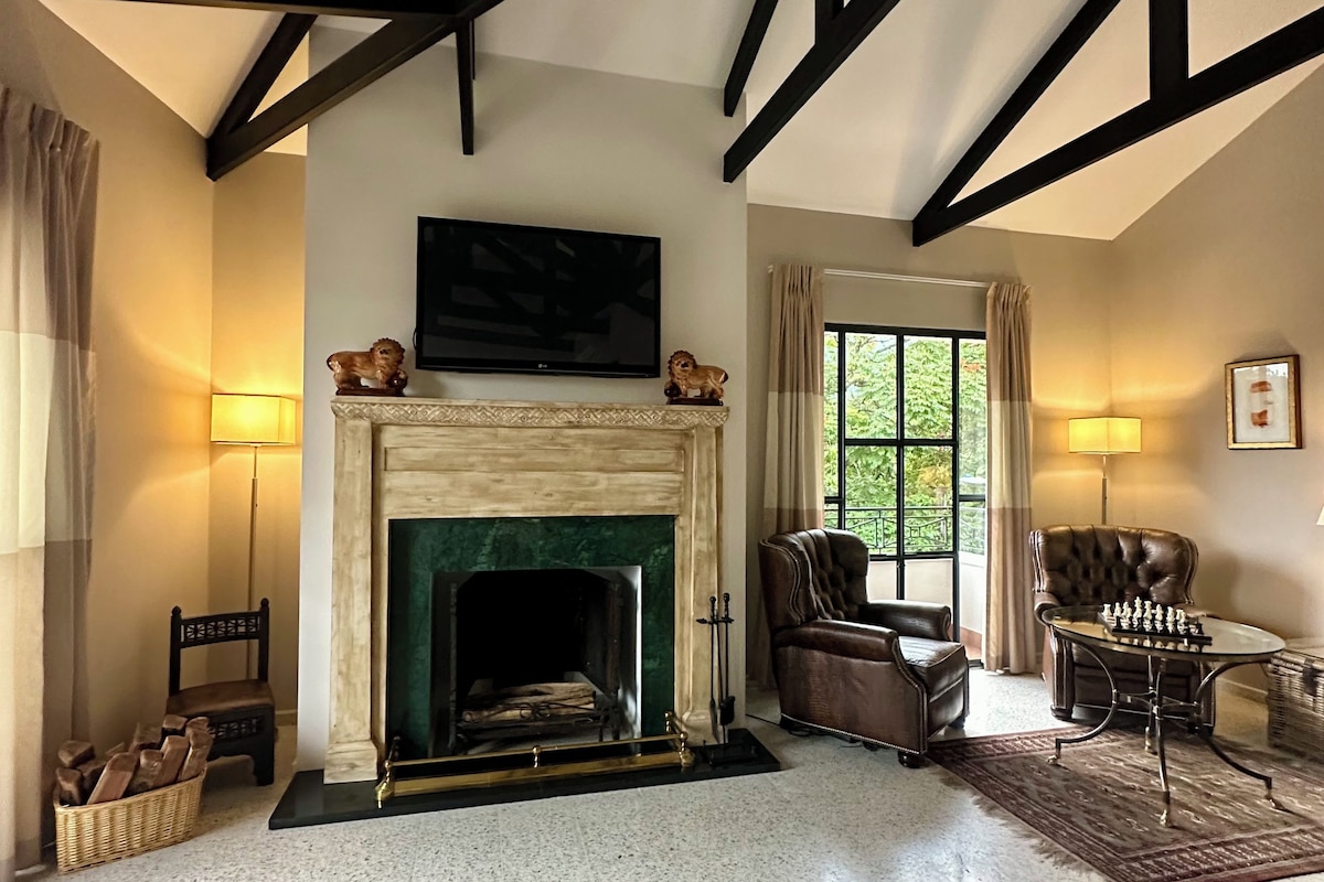 A spacious living room with a fireplace, a television mounted above it, and a chess table.