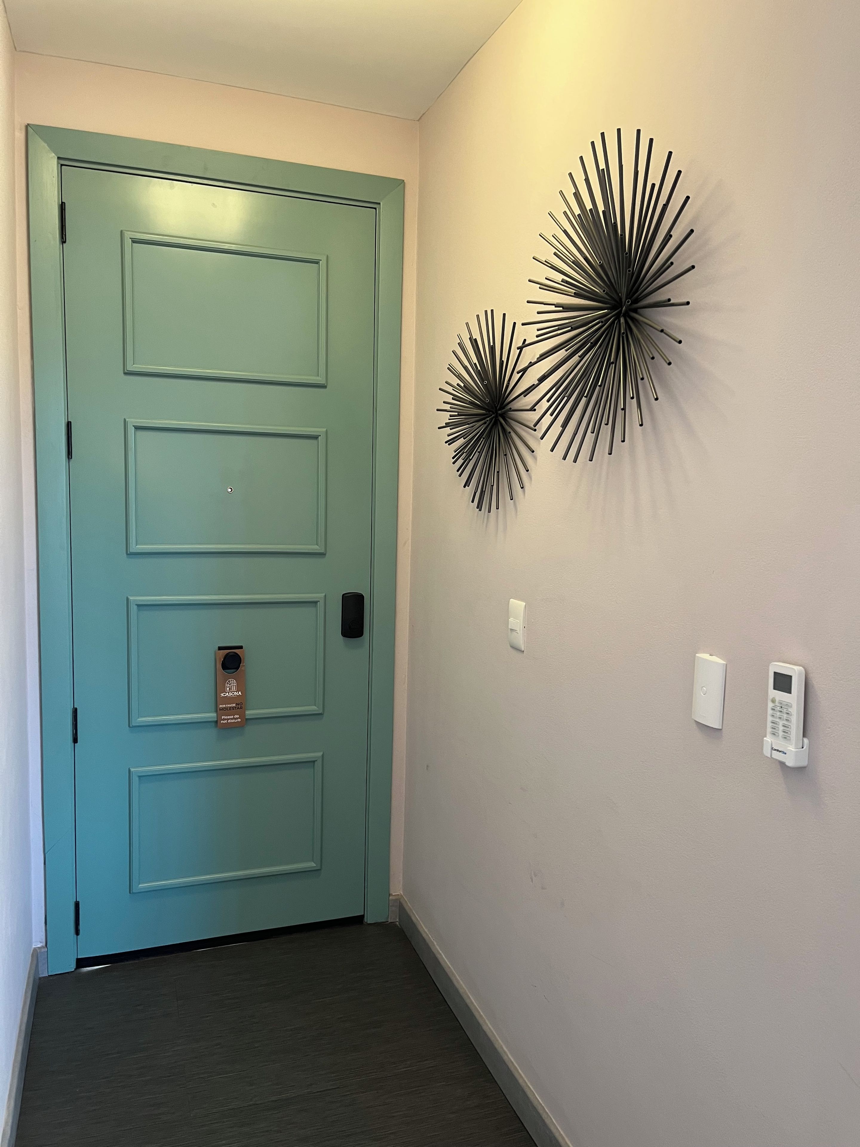 A teal door with a card reader, two wall-mounted light fixtures, and a wall-mounted thermostat.