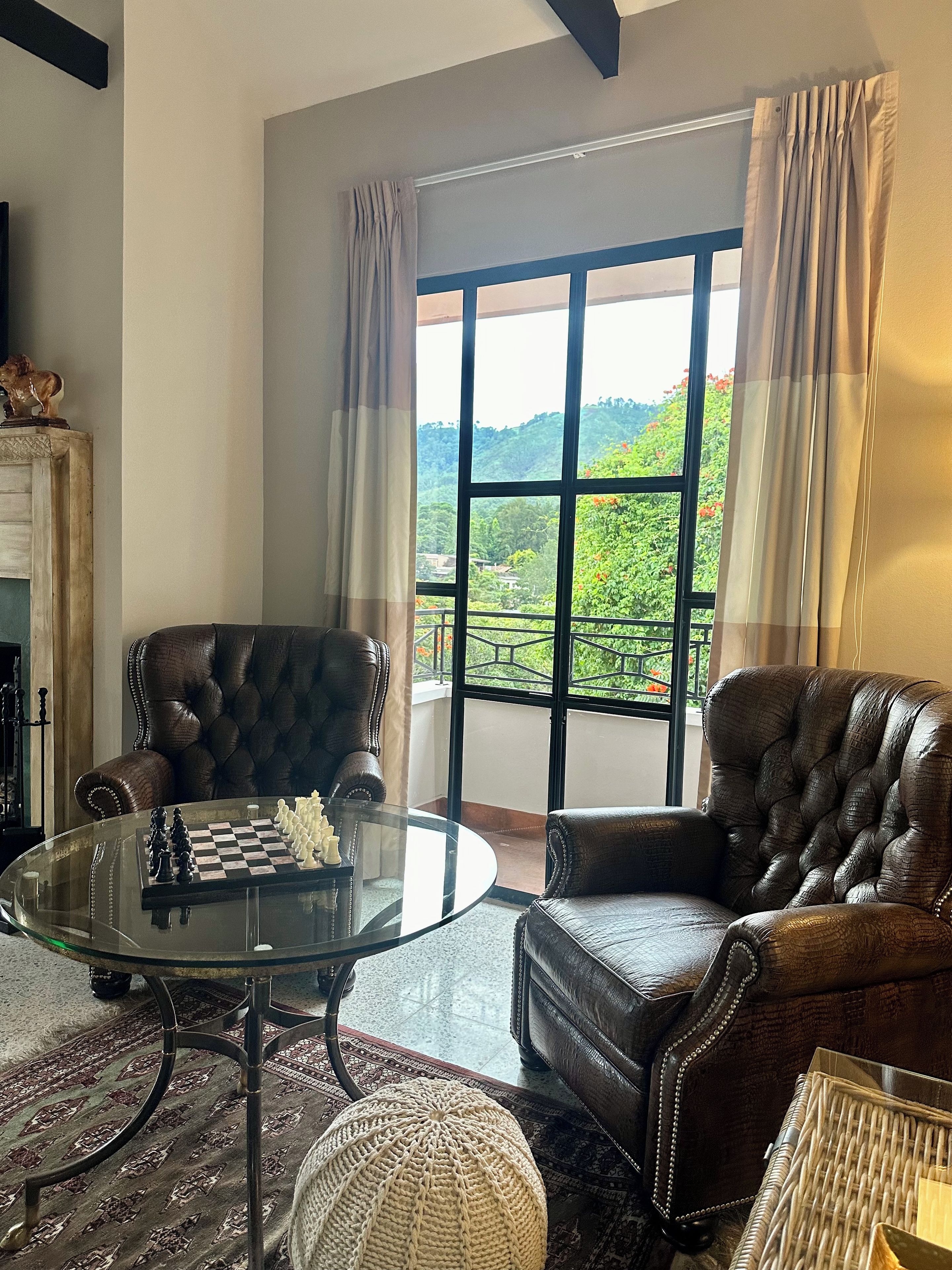 Una sala de estar con un tablero de ajedrez, sillones de cuero, una mesa de centro de vidrio, una chimenea y vistas a la vegetación a través de amplios ventanales.