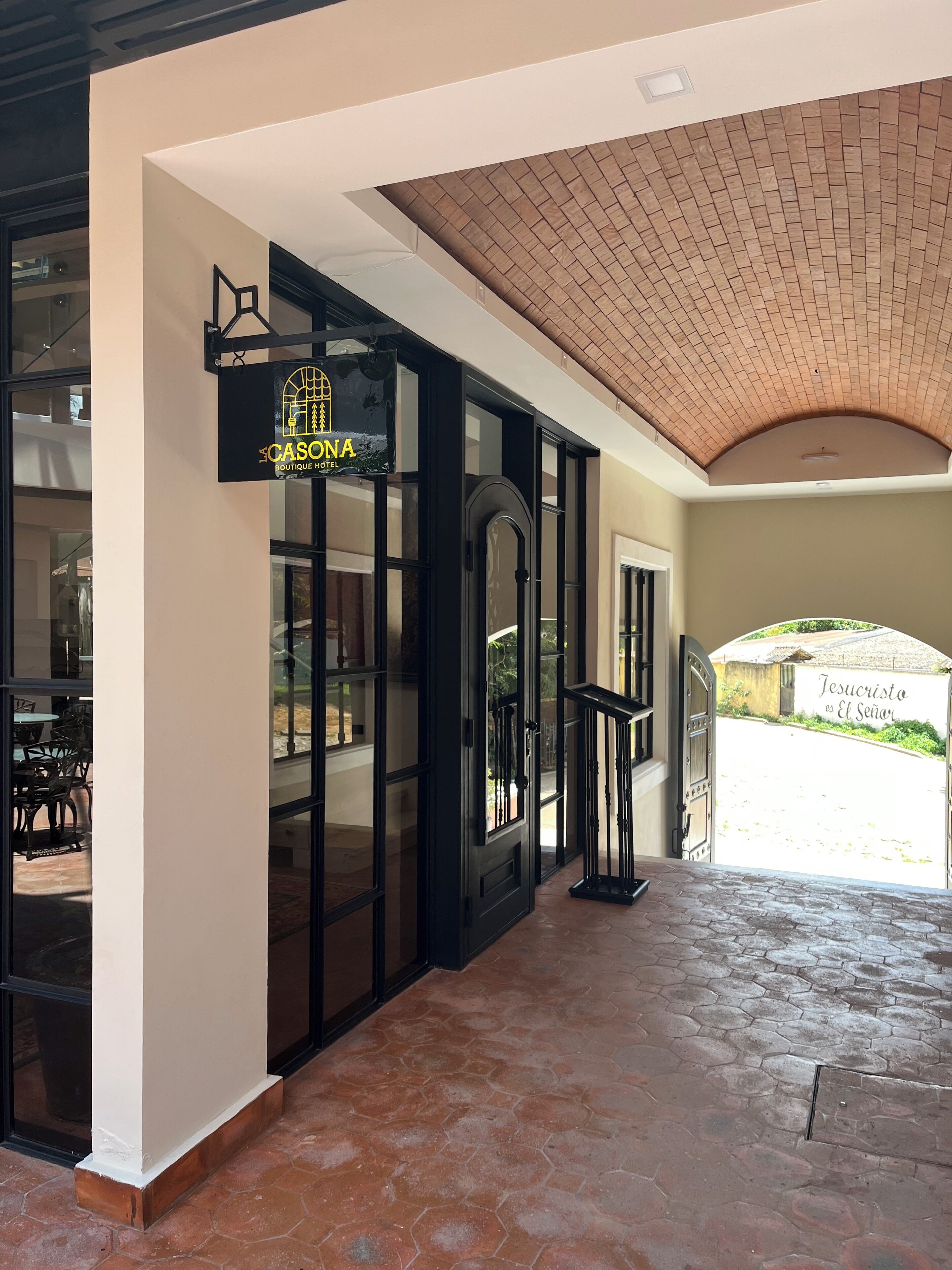 Een hotelentree met een bord waarop 'CASONA Boutique Hotel' staat, een betegeld dak en een uitzicht op de straat.