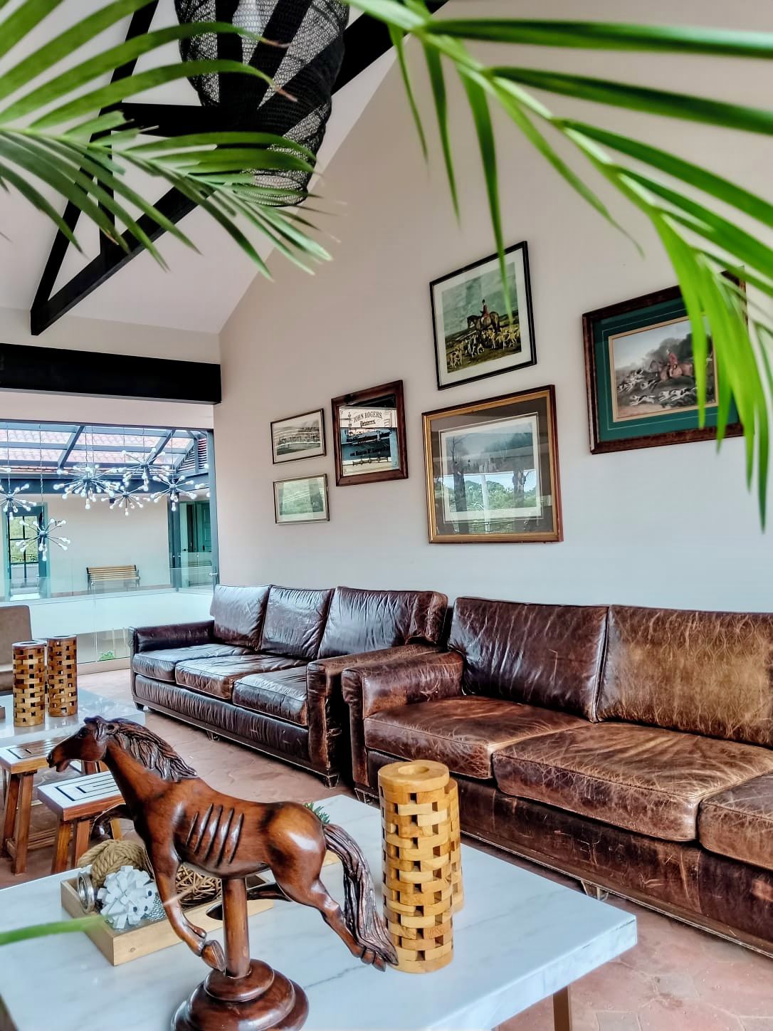 A spacious living room with a brown leather sofa, a wooden horse sculpture, and a coffee table.
