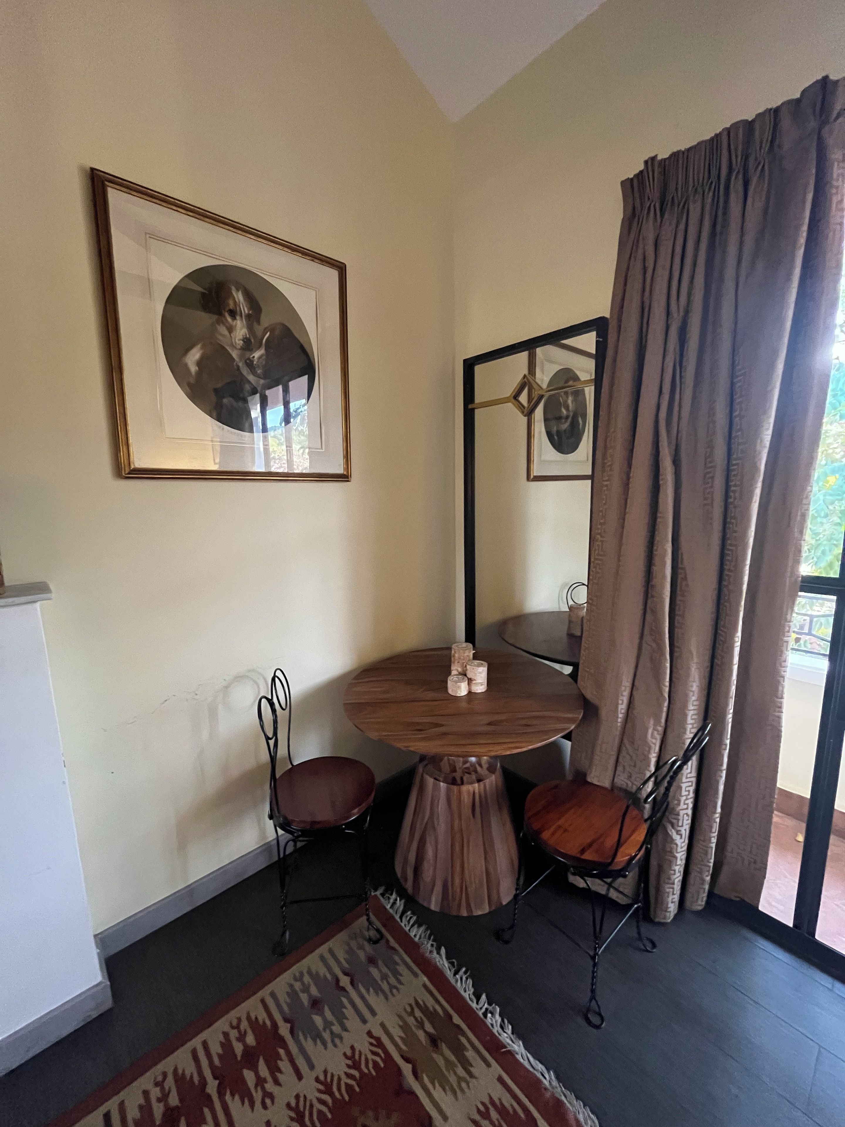 A dining area with a round wooden table, two chairs, a framed picture on the wall, and a patterned rug.