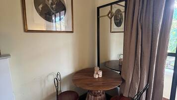 A dining area with a round wooden table, two chairs, a framed picture on the wall, and a patterned rug.