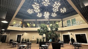 A spacious indoor area with multiple tables and chairs, a high ceiling with decorative lighting, and a central plant arrangement.