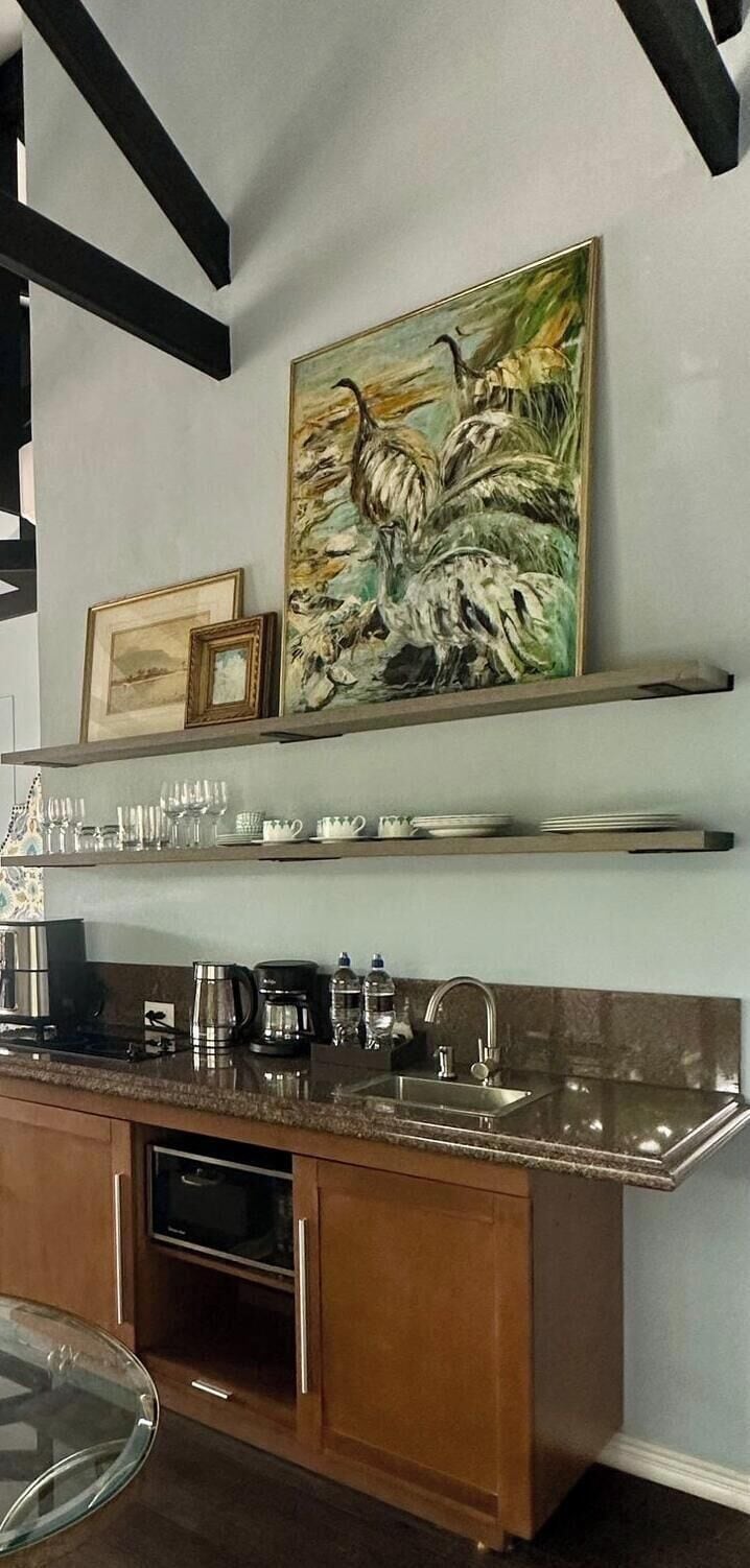A kitchen with a marble countertop, stainless steel appliances, and a painting above the sink.