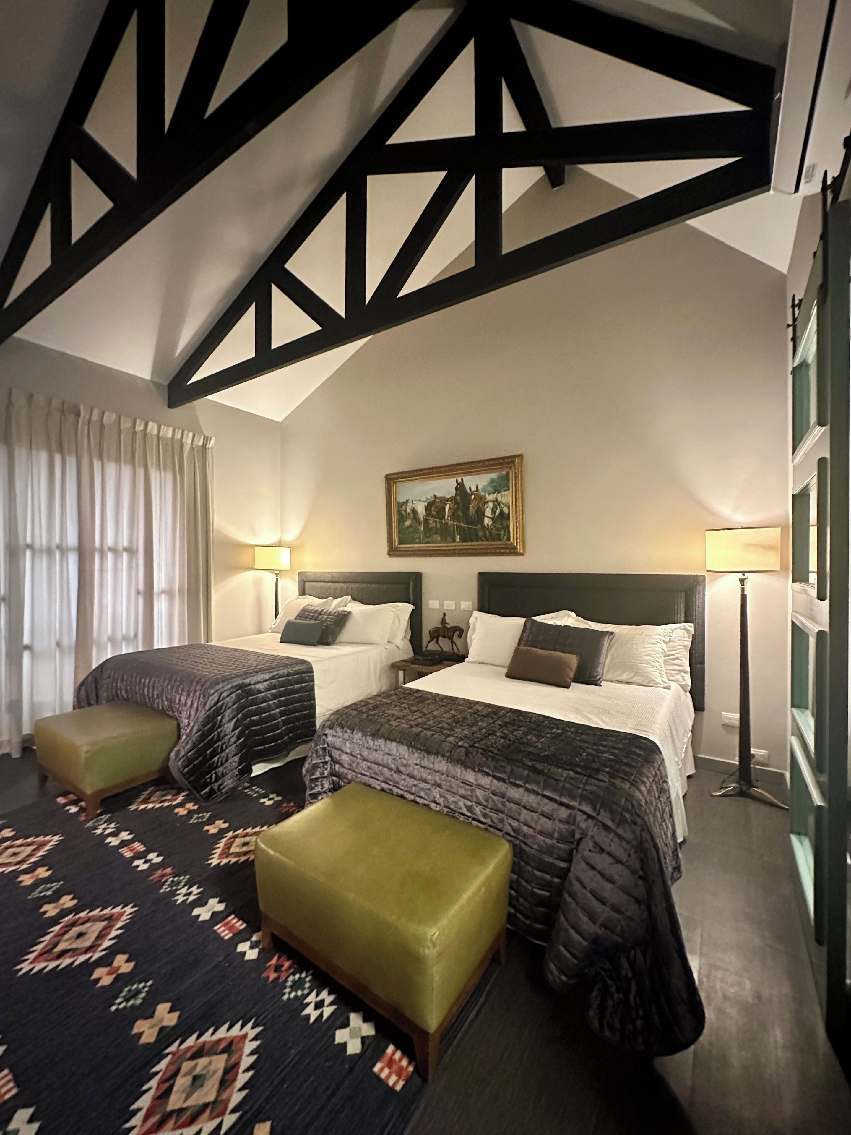A hotel room with two beds, a large window, a painting on the wall, and a patterned rug.