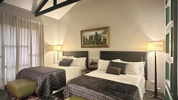 A hotel room with two beds, a large window, a painting on the wall, and a patterned rug.