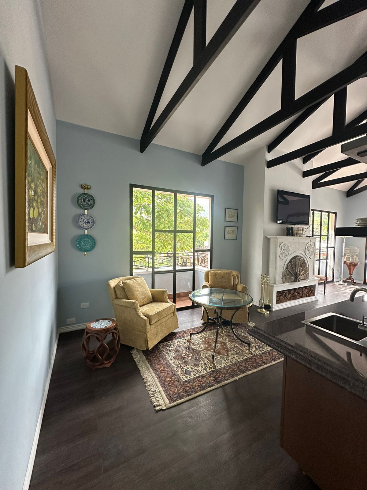 A modern living room with a glass coffee table, two armchairs, a fireplace, and a kitchen area with a sink.