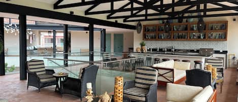Un interior moderno con barandilla de cristal, mobiliario de mimbre y una zona de cocina.