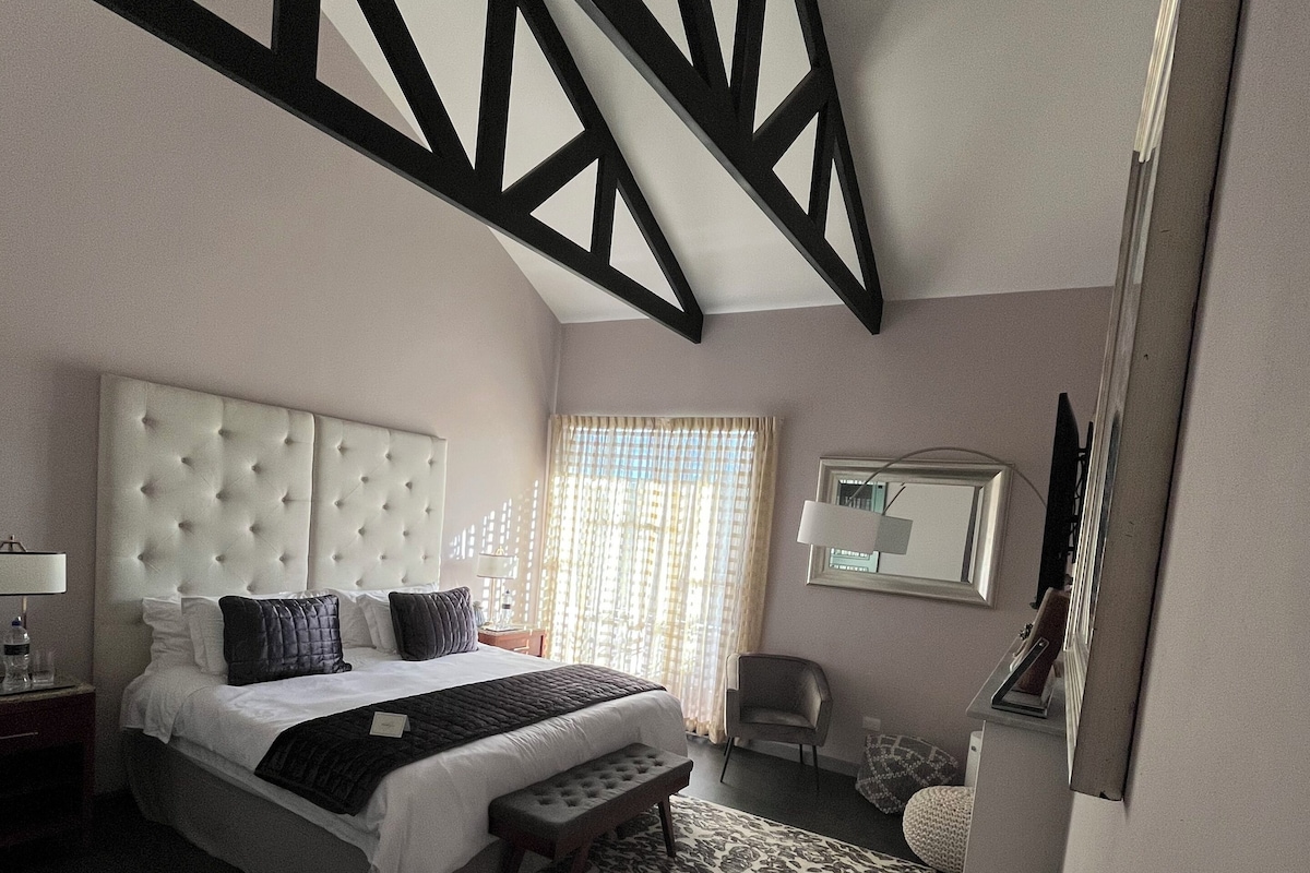 A bedroom with a large bed, a bench, a desk, and a chair.