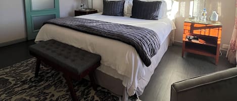 A bedroom with a large bed, a bench, a nightstand, and a window.