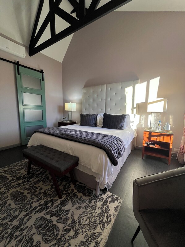 A bedroom with a large bed, a bench, a nightstand, and a window.
