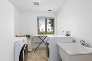 Ein Waschraum mit zwei Waschmaschinen, einem Waschbecken und einem Fenster mit Blick auf ein Haus.