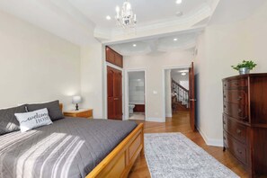 Ein Schlafzimmer mit Bett, Nachttisch, Kommode und einem zur Toilette führenden Flur.