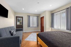 A bedroom with a bed, a sofa, a door, and windows. - Nordhaus | Walk to Beach | Hot Tub | Private Yard! (South Haven)