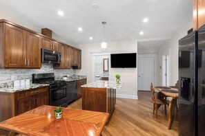 A modern kitchen with wooden cabinets, a granite countertop, and stainless steel appliances. - Nordhaus | Walk to Beach | Hot Tub | Private Yard! (South Haven)