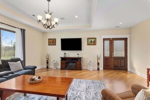 A living room with a sofa, a coffee table, a fireplace, a television, and a door. - Nordhaus | Walk to Beach | Hot Tub | Private Yard! (South Haven)