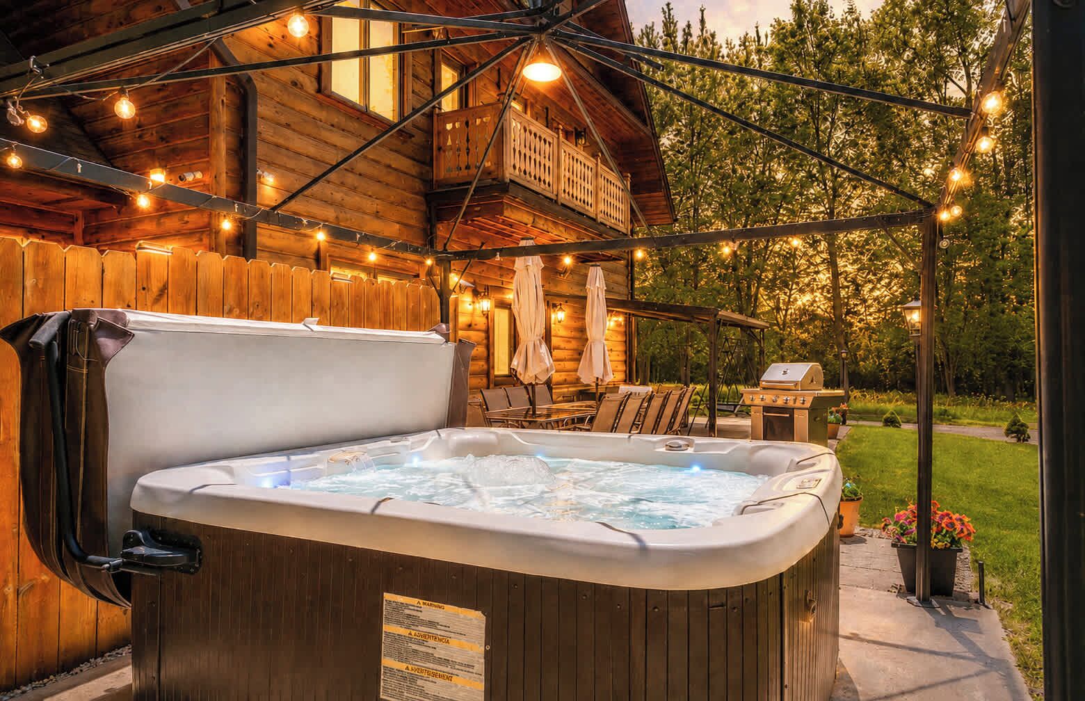 Ein Außenbereich mit Whirlpool, Holzterrasse, Liegestühlen und Lichterketten.