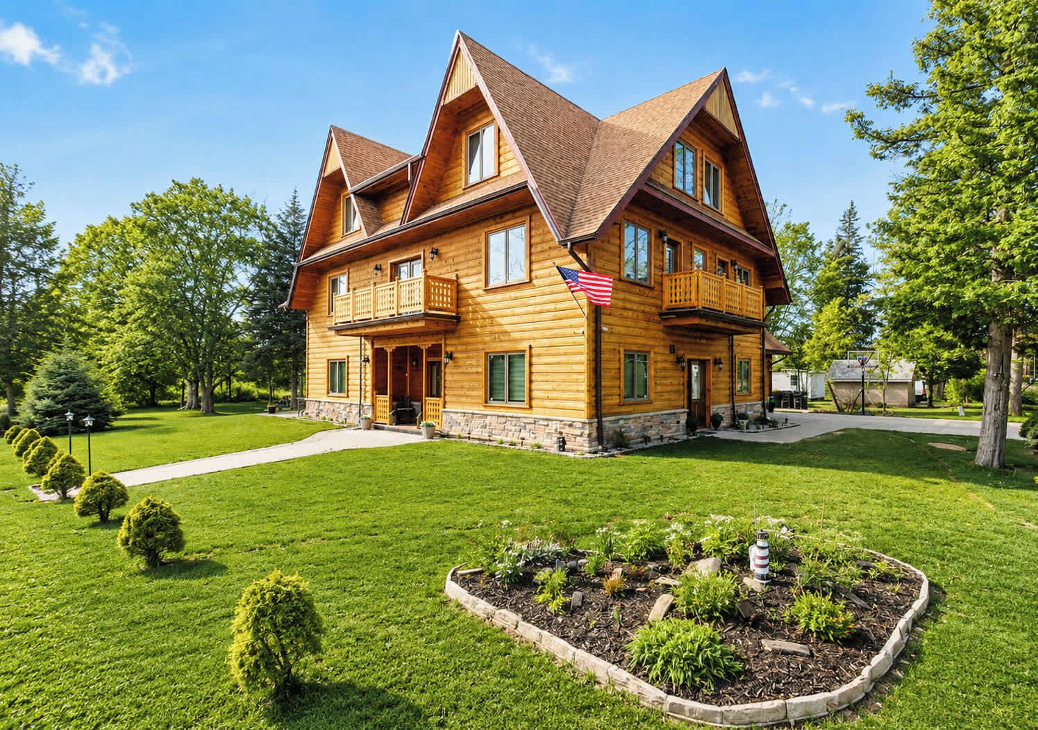 A two-story wooden house with a balcony, surrounded by a well-maintained lawn and a small garden.