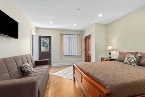 A bedroom with a bed, a sofa, a bedside table with a lamp, a window with curtains, and a door. - Nordhaus | Walk to Beach | Hot Tub | Private Yard! (South Haven)