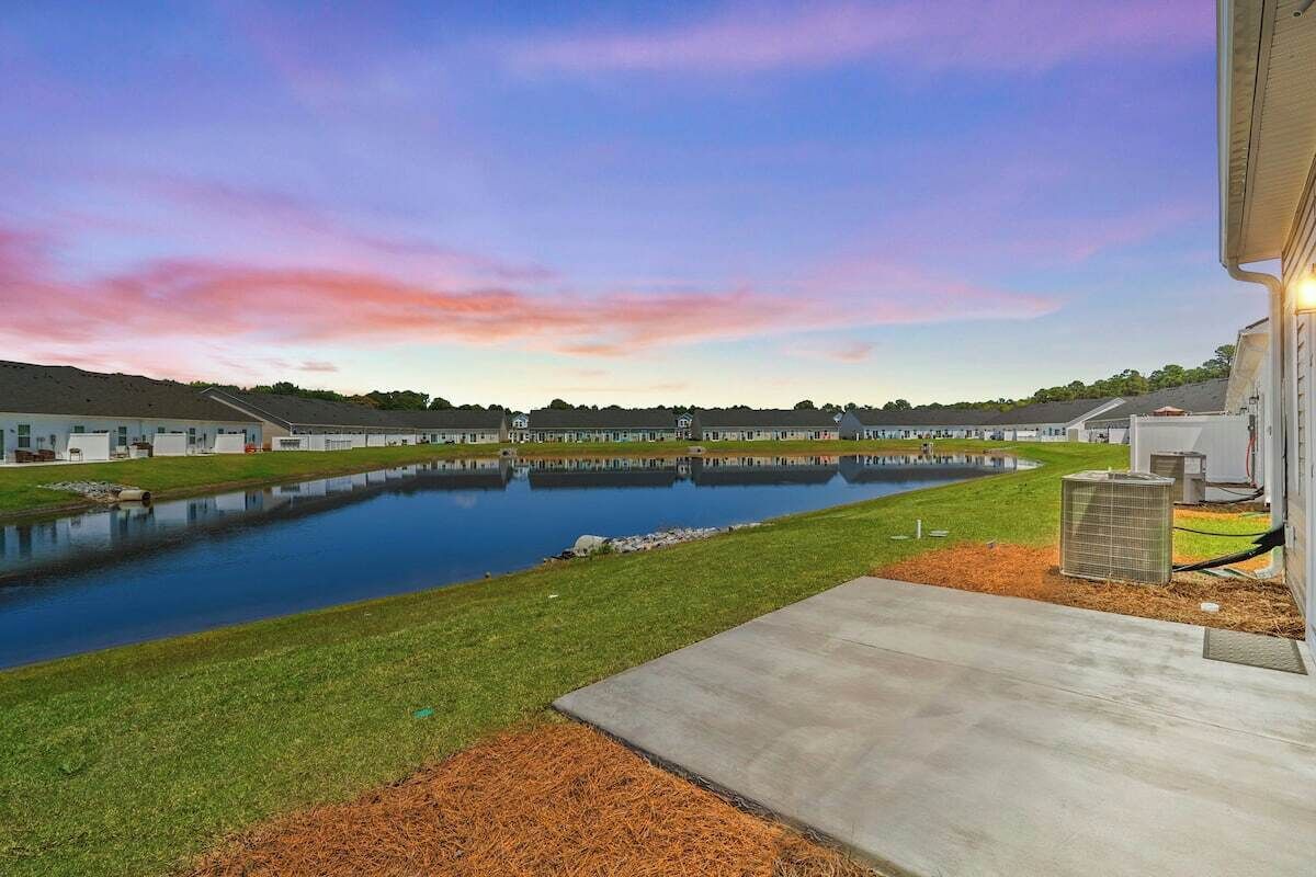 A residential area with a large pond, a grassy lawn, and a building with a flat roof.