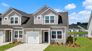 A two-story residential building with a garage, a covered driveway, and a small pond in the background. - LakeView Modern 3BR/3BA Near Beach NewBuild Home Myrtle Beach (Myrtle Beach)