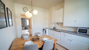 A compact kitchen with white cabinets, a wooden dining table set for two, and a microwave on the countertop.