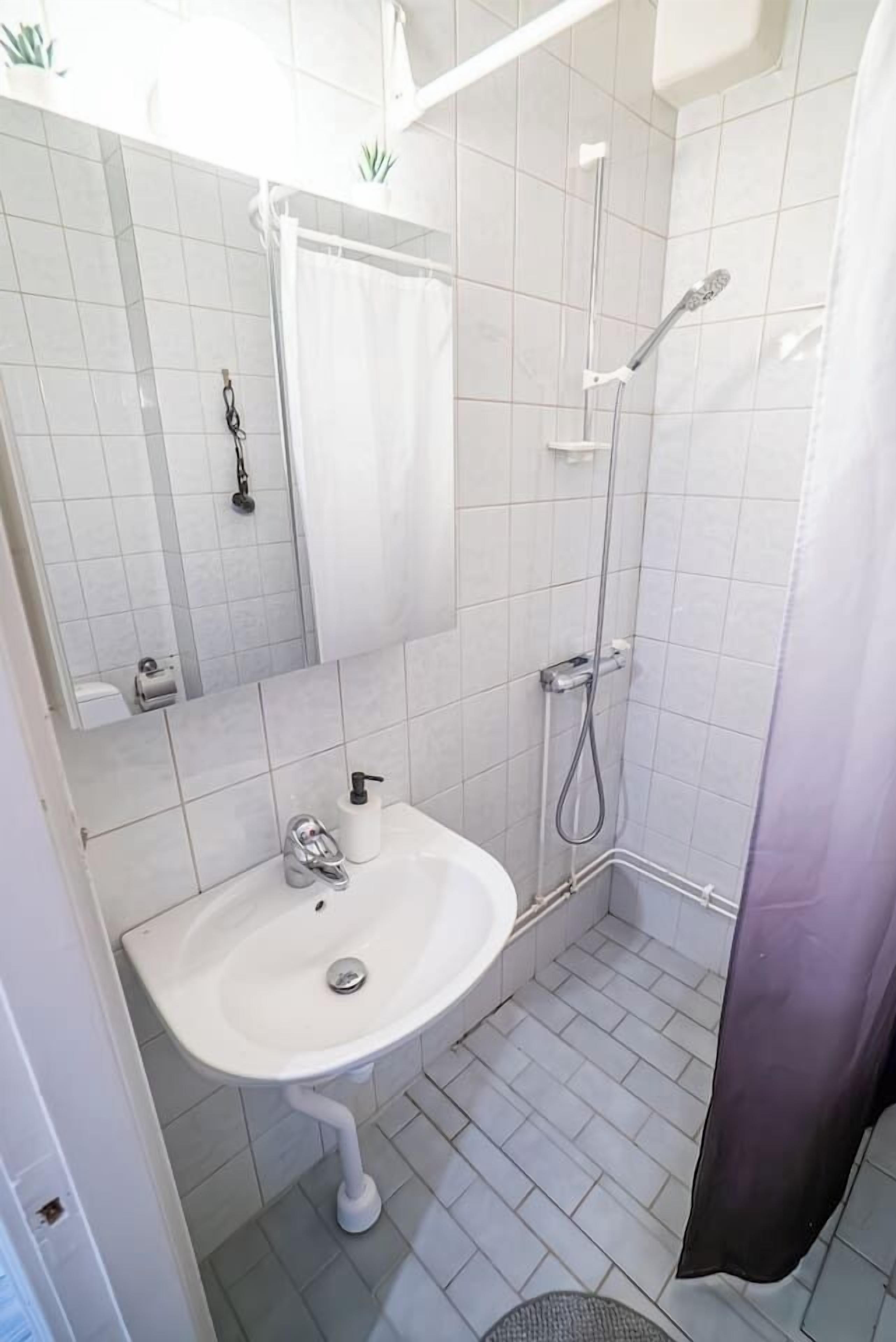 Ett badrum med ett vitt handfat, en spegel, en dusch med ett justerbart duschhuvud och en toalett.