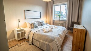 A modern bedroom with a bed, bedside tables, a window with curtains, a radiator, and a view of the city.