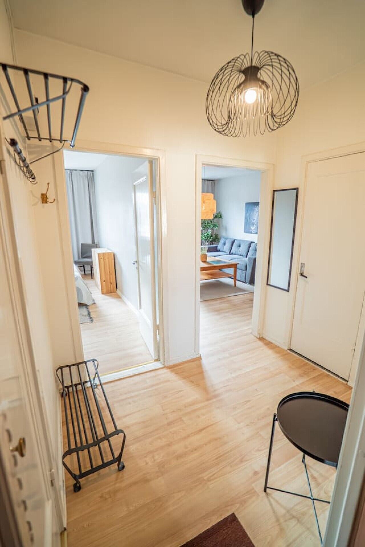 A hallway with a wooden floor, a black chair, a metal rack, and a hanging light fixture.