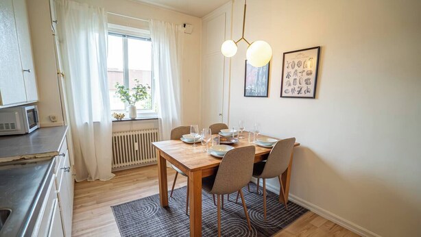 A dining area with a wooden table, four chairs, and a hanging light fixture.
