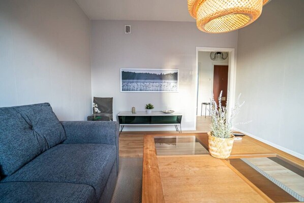 A modern living room with a grey sofa, a wooden coffee table, a console table with decorative items, and a large framed picture on the wall.